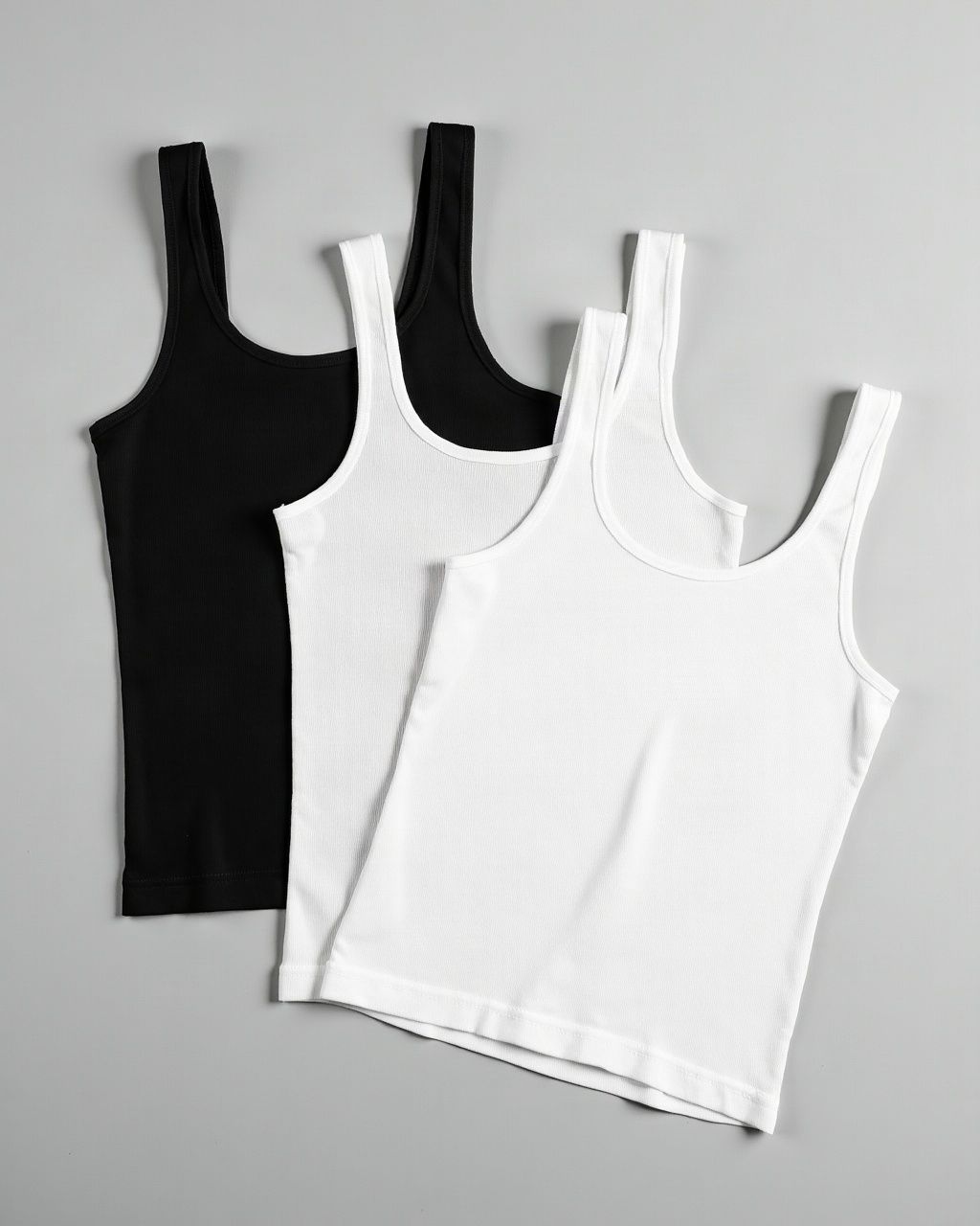 Three ribbed tank tops laid flat: one black, two white